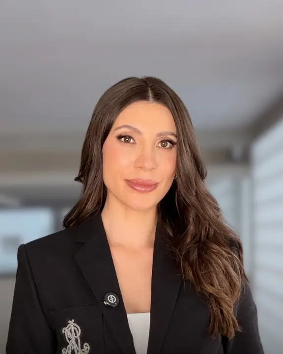 Melina Verona, de blazer preto, olhando para a câmera