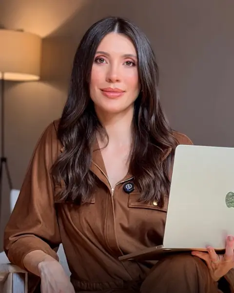 Melina Verona sentada, de roupa marrom, com um notebook